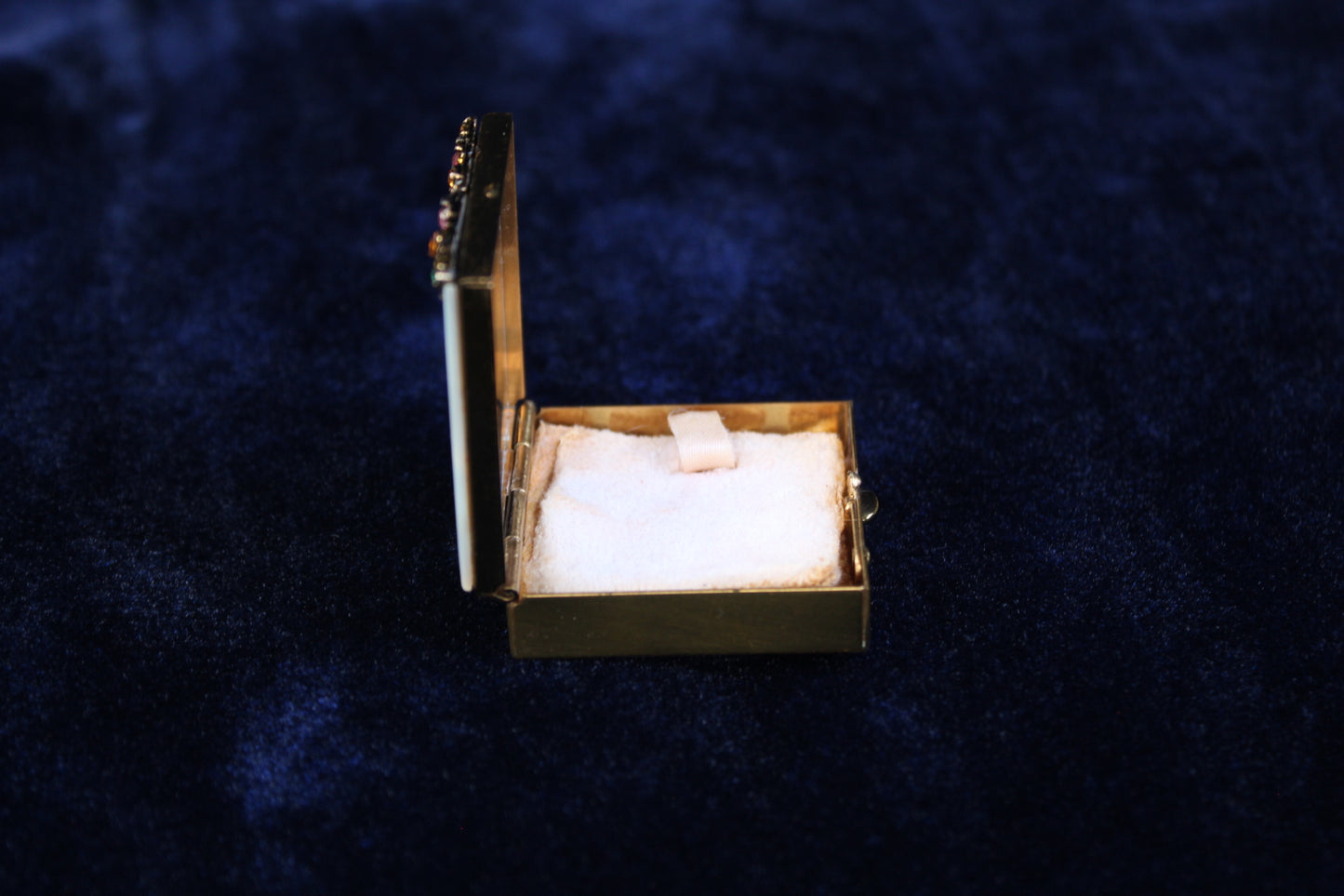 Gold filigree compact with mother-of-pearl lid and rhinestones, open to reveal powder compartment.