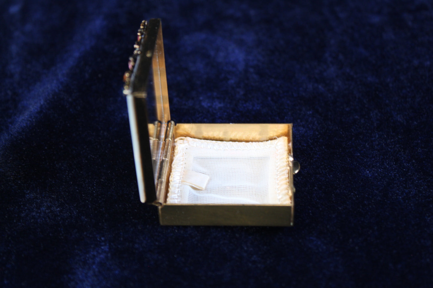 Gold filigree powder case with mother of pearl lid, open to show white powder puff and mirror.