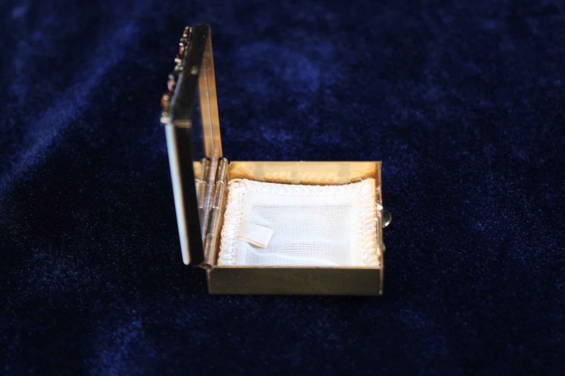 Gold filigree powder case with mother of pearl lid, open to show white powder puff and mirror.