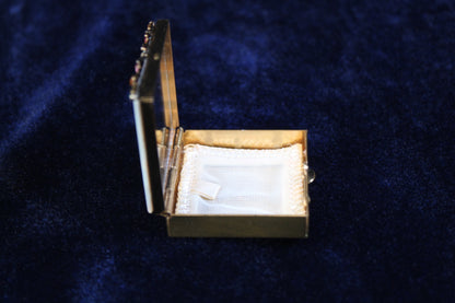 Gold filigree powder case with mother of pearl lid, open to show white powder puff and mirror.