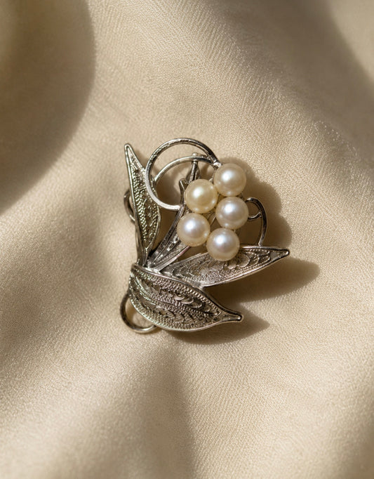 Silver-tone floral spray brooch with five faux pearls on a cream fabric background.