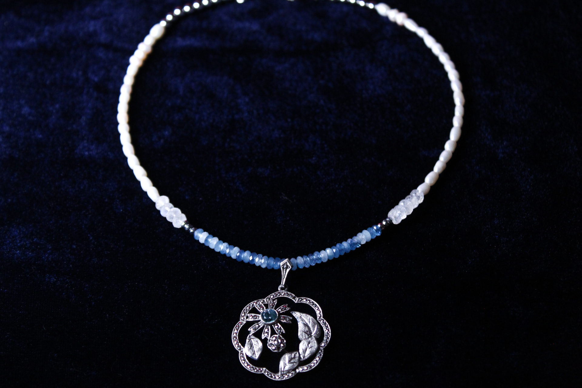 Sterling silver pendant necklace with aquamarine and moonstone beads on a dark blue background.